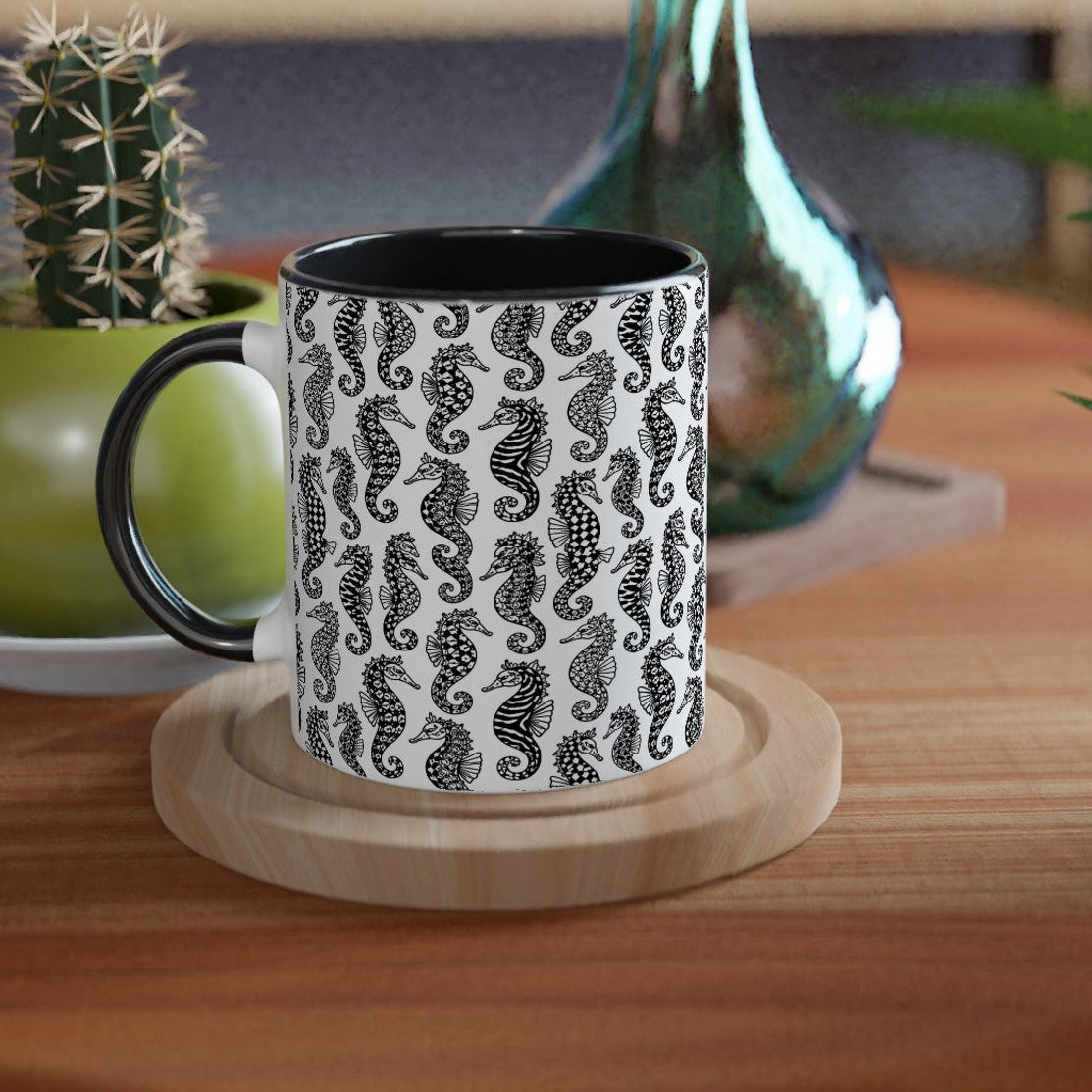 Black and white patterned mug on a wooden coaster with a plant and vase in the background.