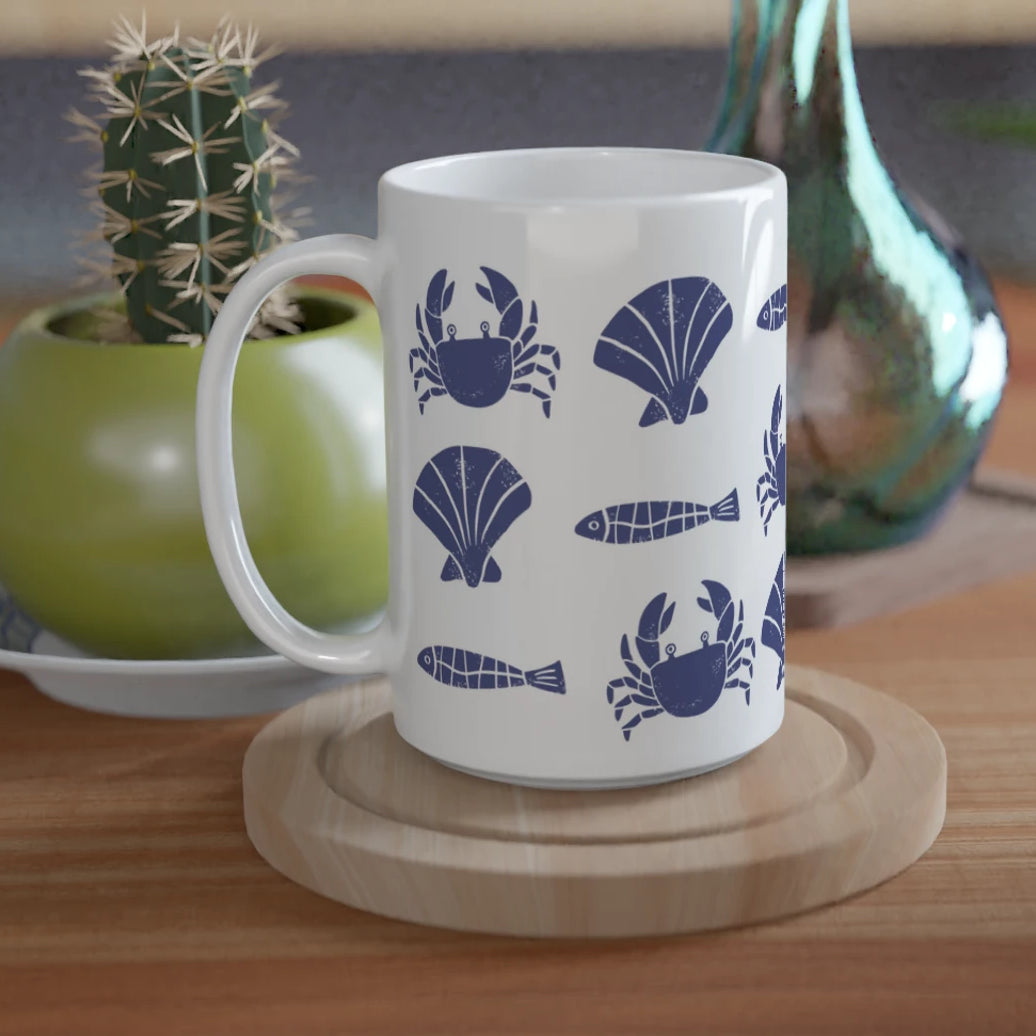 White mug with blue sea-themed design on a wooden table with plants and a green vase.
