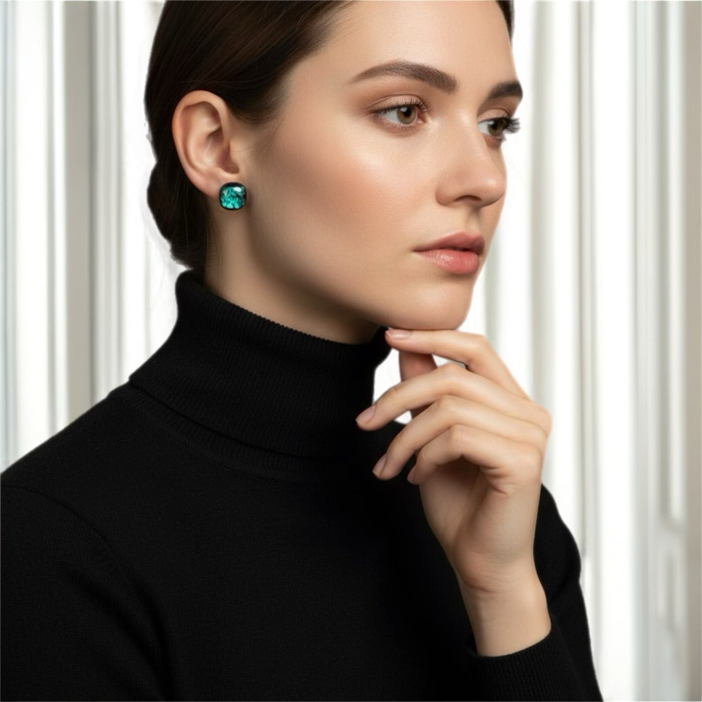 Woman wearing a black turtleneck and green earrings against a white background
