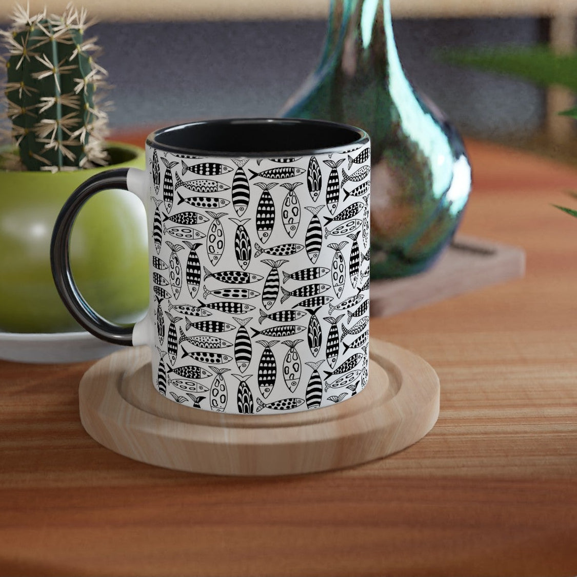 Black mug with white pattern on a wooden table with plants and a vase.