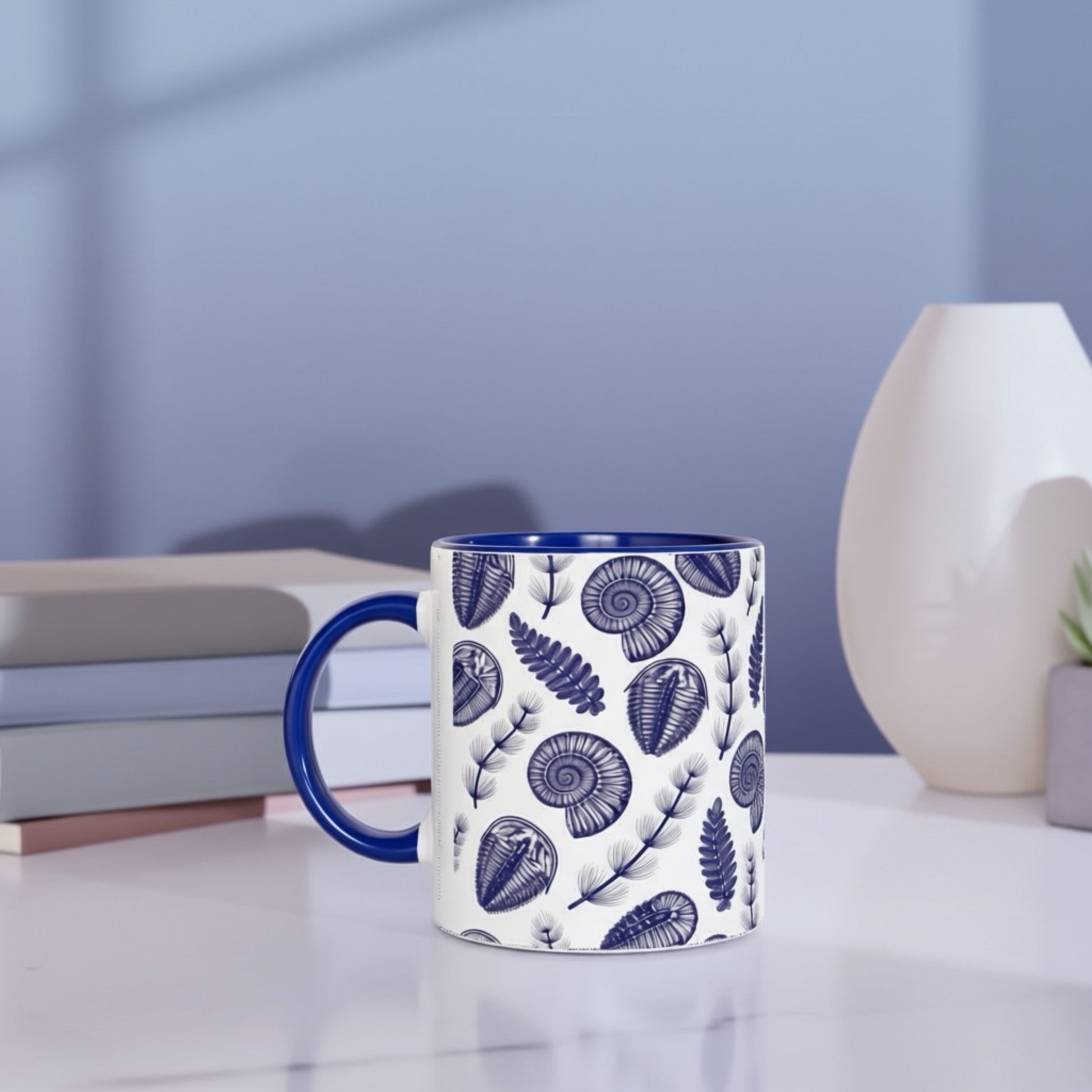 Mug with blue floral pattern on a white surface with books and a vase in the background