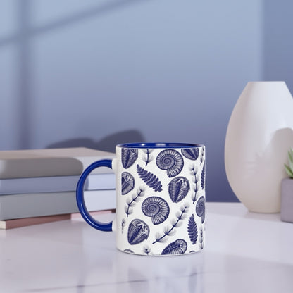 Mug with blue floral pattern on a white surface with books and a vase in the background