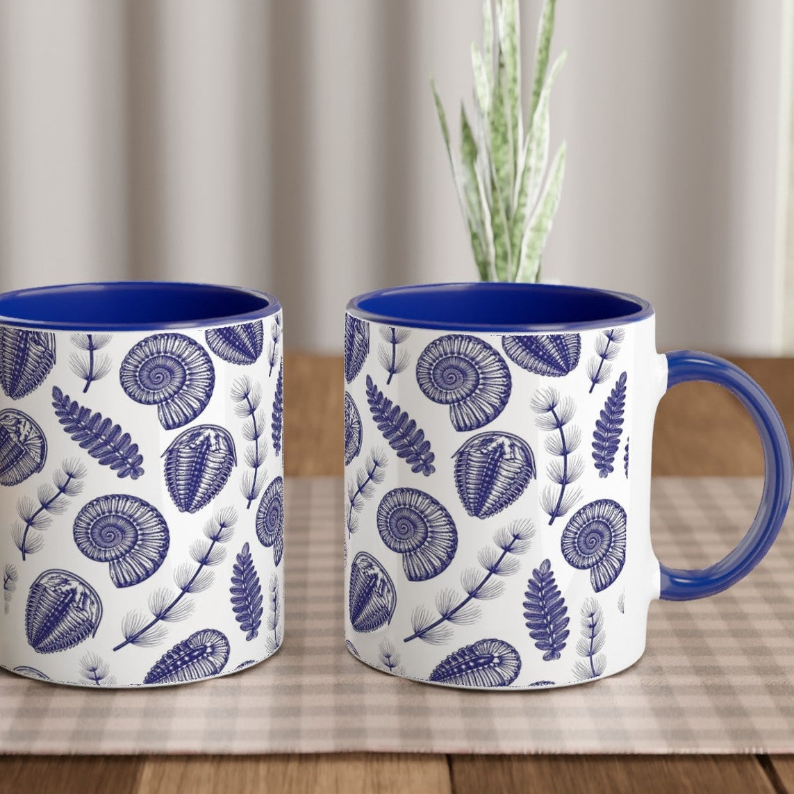 Two blue and white patterned mugs on a wooden table with a checkered tablecloth.