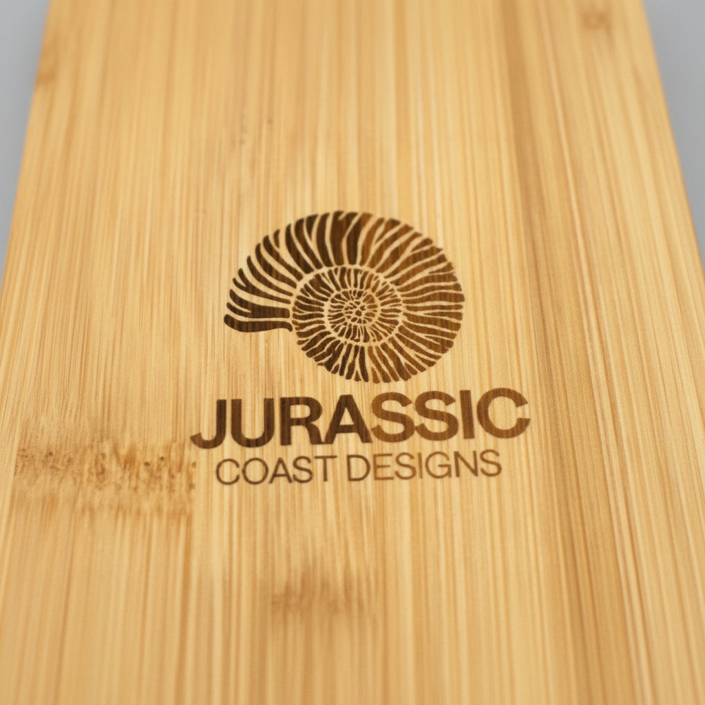 Bamboo surface with 'Jurassic Coast Designs' logo engraved.