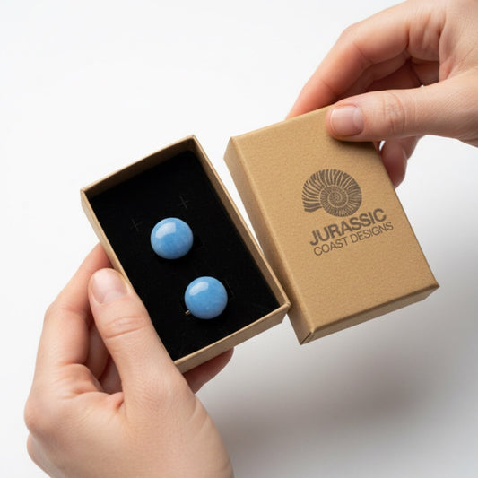Blue cufflinks in a 'Jurassic Coast Designs' box held by hands on a light background