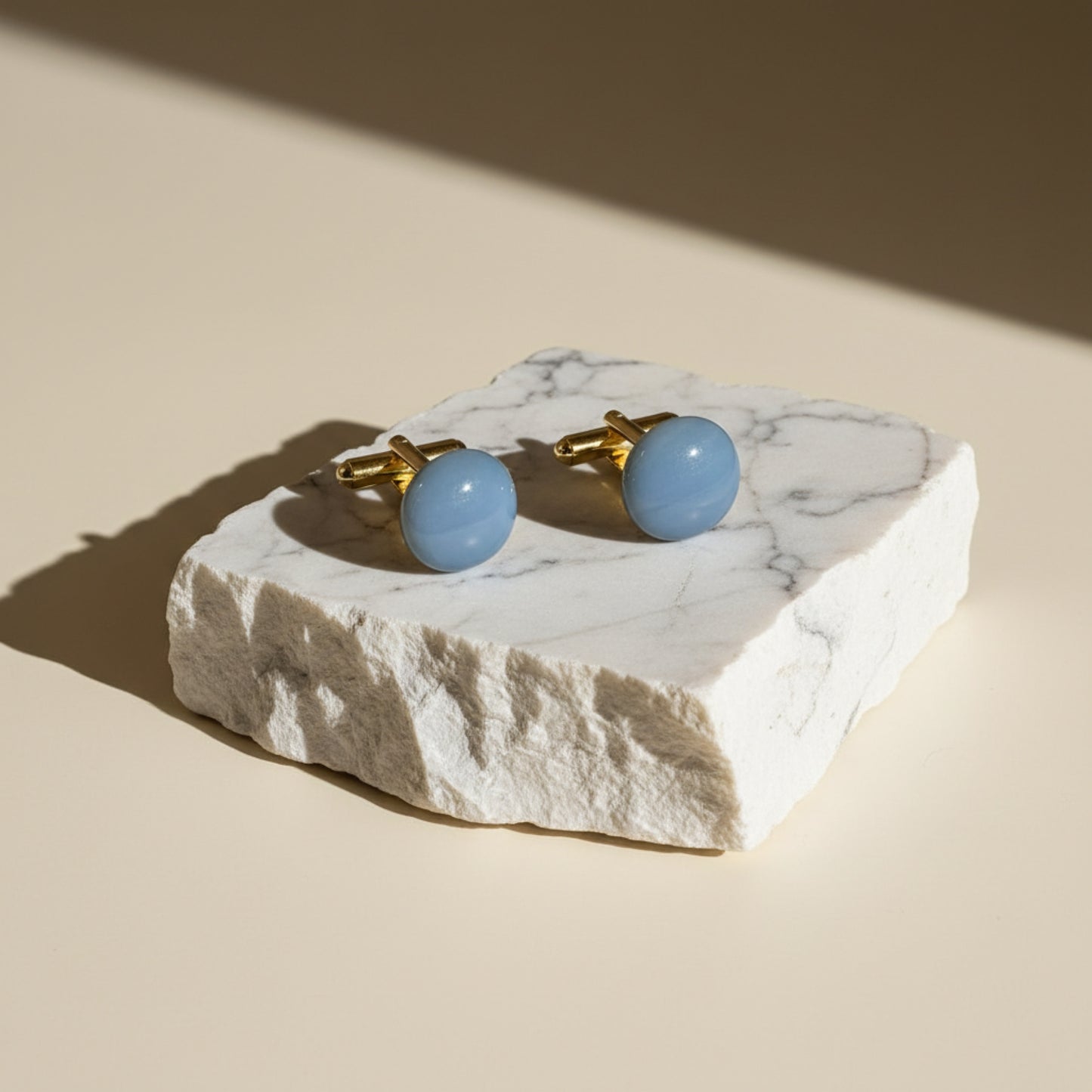 Cufflinks with blue stones on a marble stand against a beige background