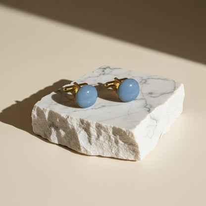 Cufflinks with blue stones on a marble stand against a beige background