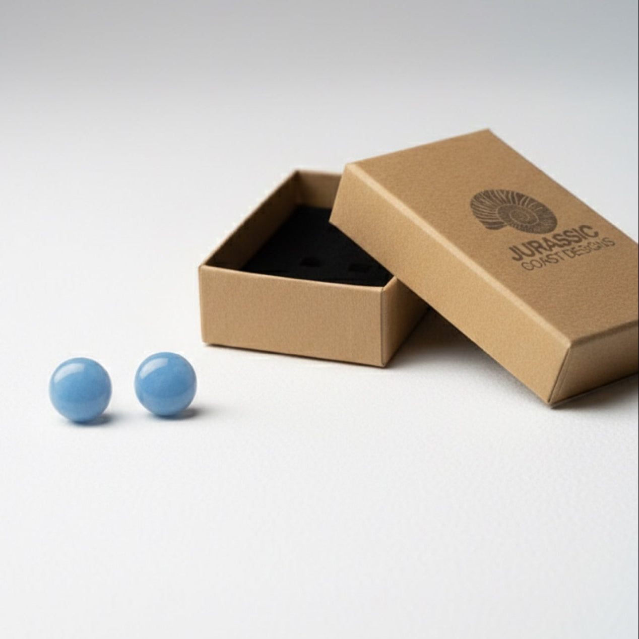 Blue cufflinks in an open brown box on a light gray background