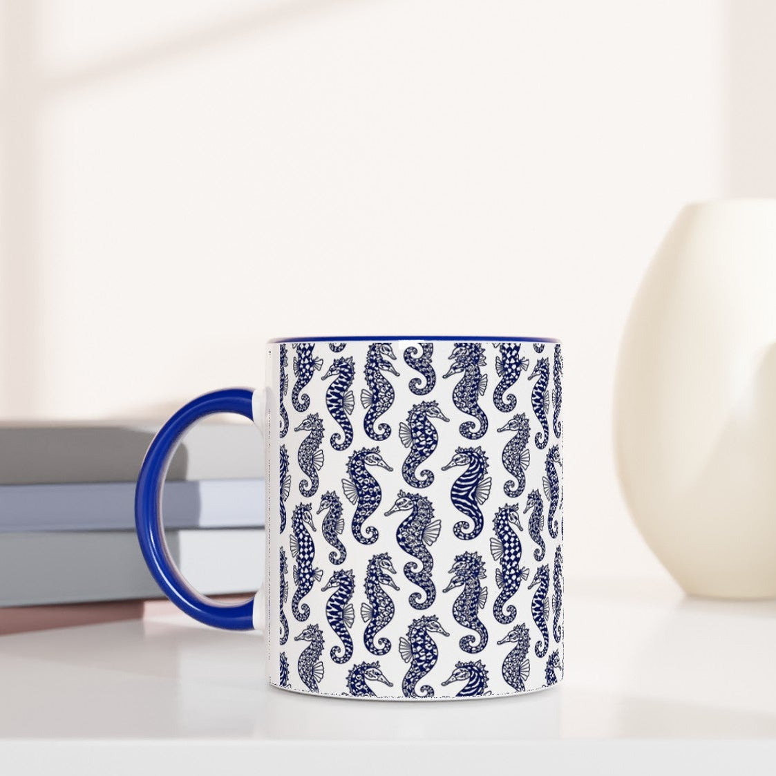 Mug with seahorse pattern on a white surface with books and decorative items.