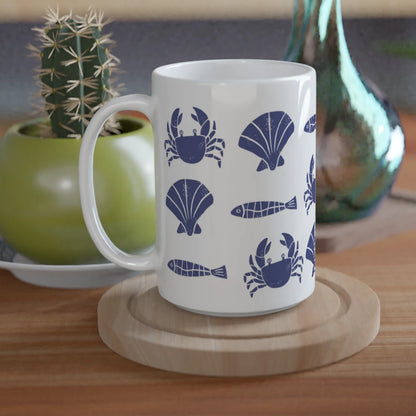 White mug with blue sea-themed design on a wooden table with plants and a green vase.