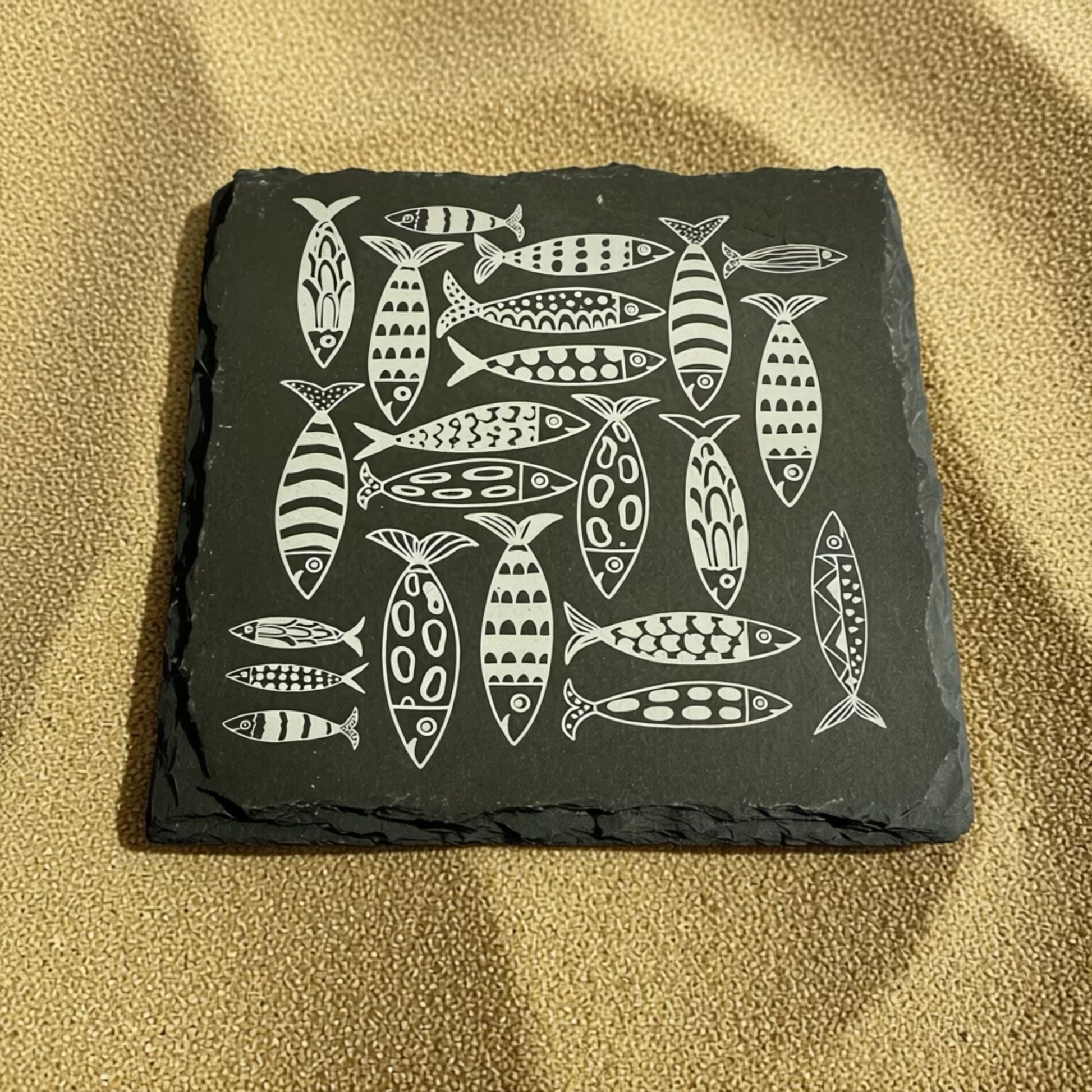 Slate coaster with fish pattern on a beige surface