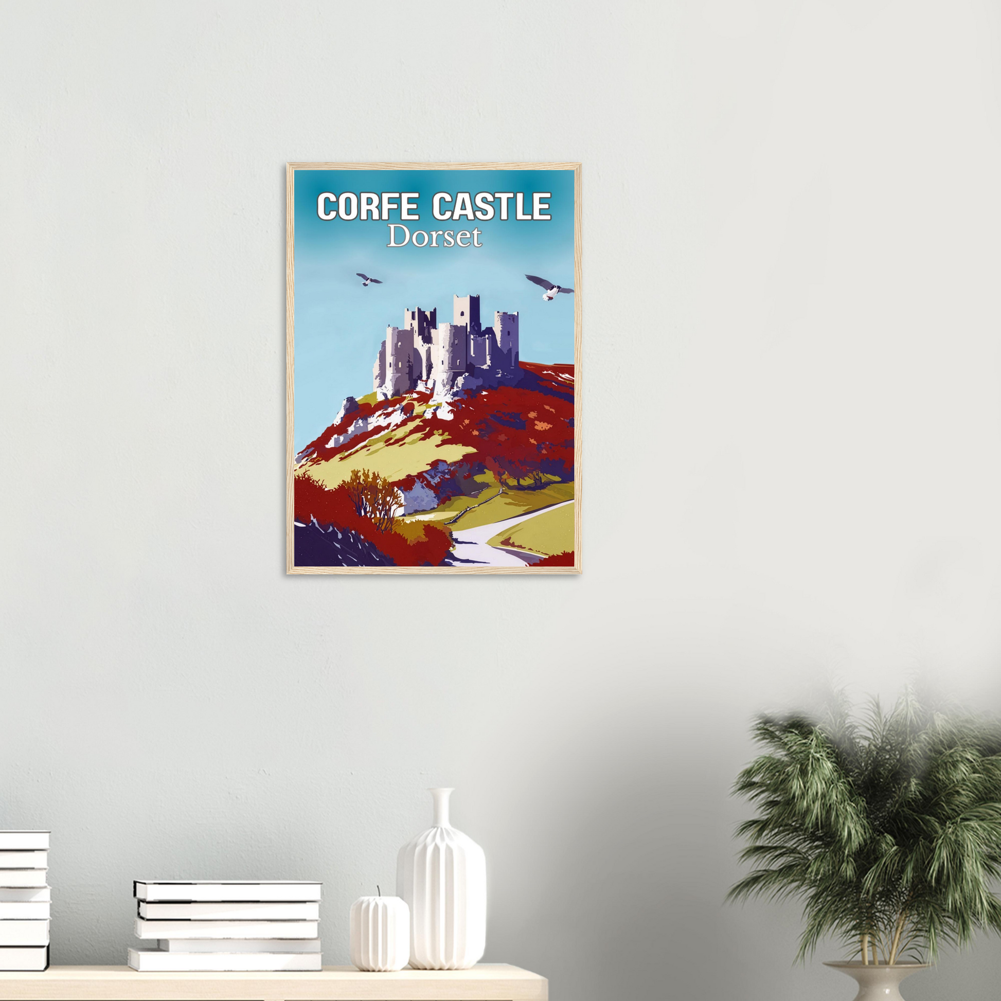 Framed poster of Corfe Castle, Dorset on a wall with decor items below.