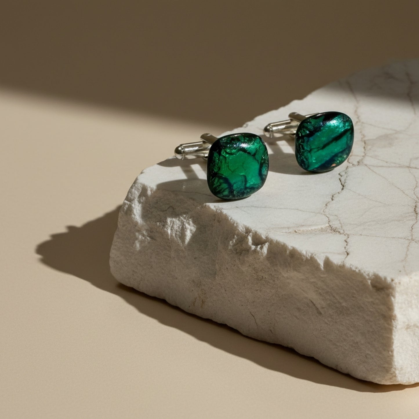 Green glass cufflinks on a white marble block with a beige background