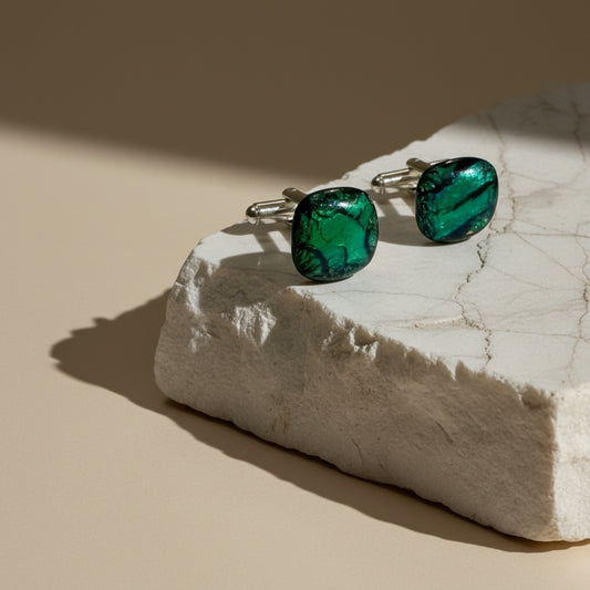 Green glass cufflinks on a white marble block with a beige background
