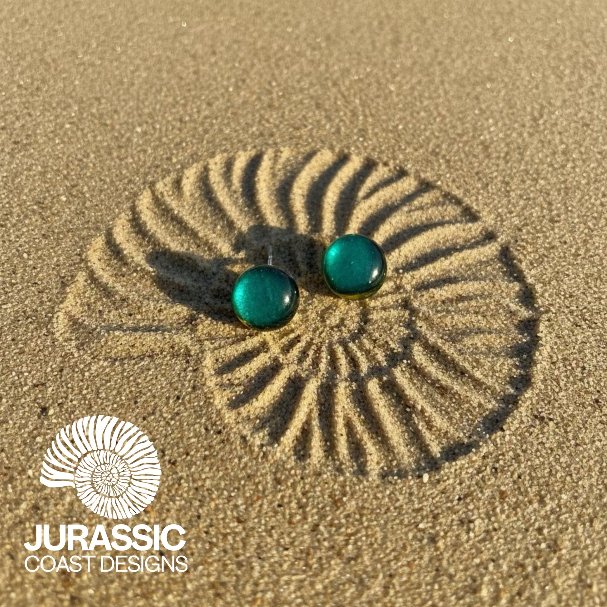 Turquoise earrings on sand with 'Jurassic Coast Designs' logo.