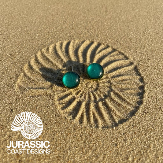 Turquoise earrings on sand with 'Jurassic Coast Designs' logo.