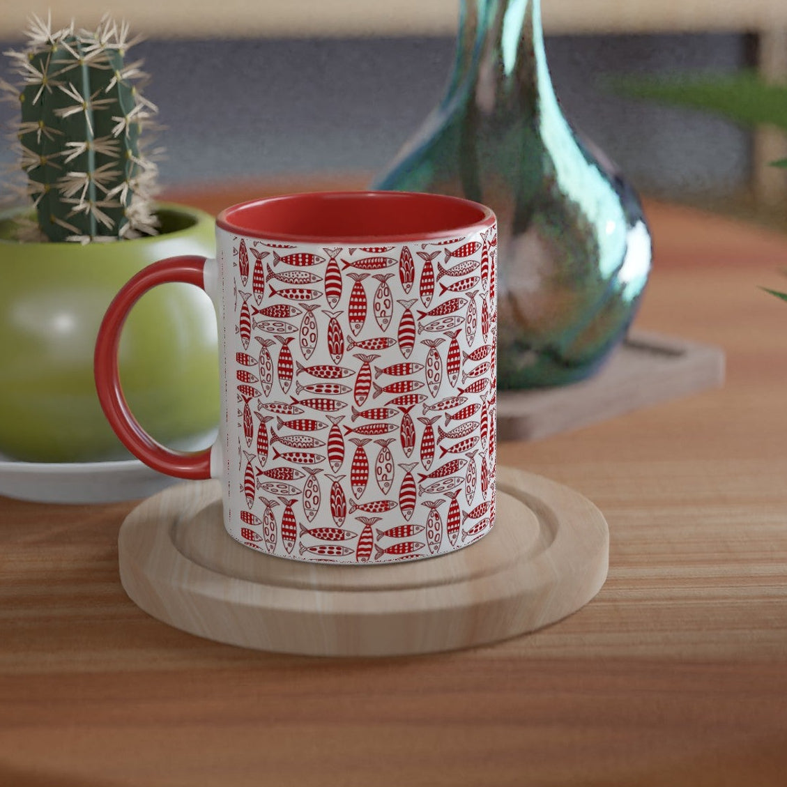 Red mug with white pattern on a wooden table with plants and a vase.