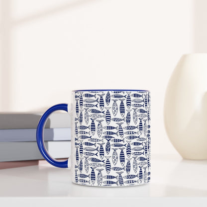 Mug with blue handle and white pattern on a white surface with books and decorative items.