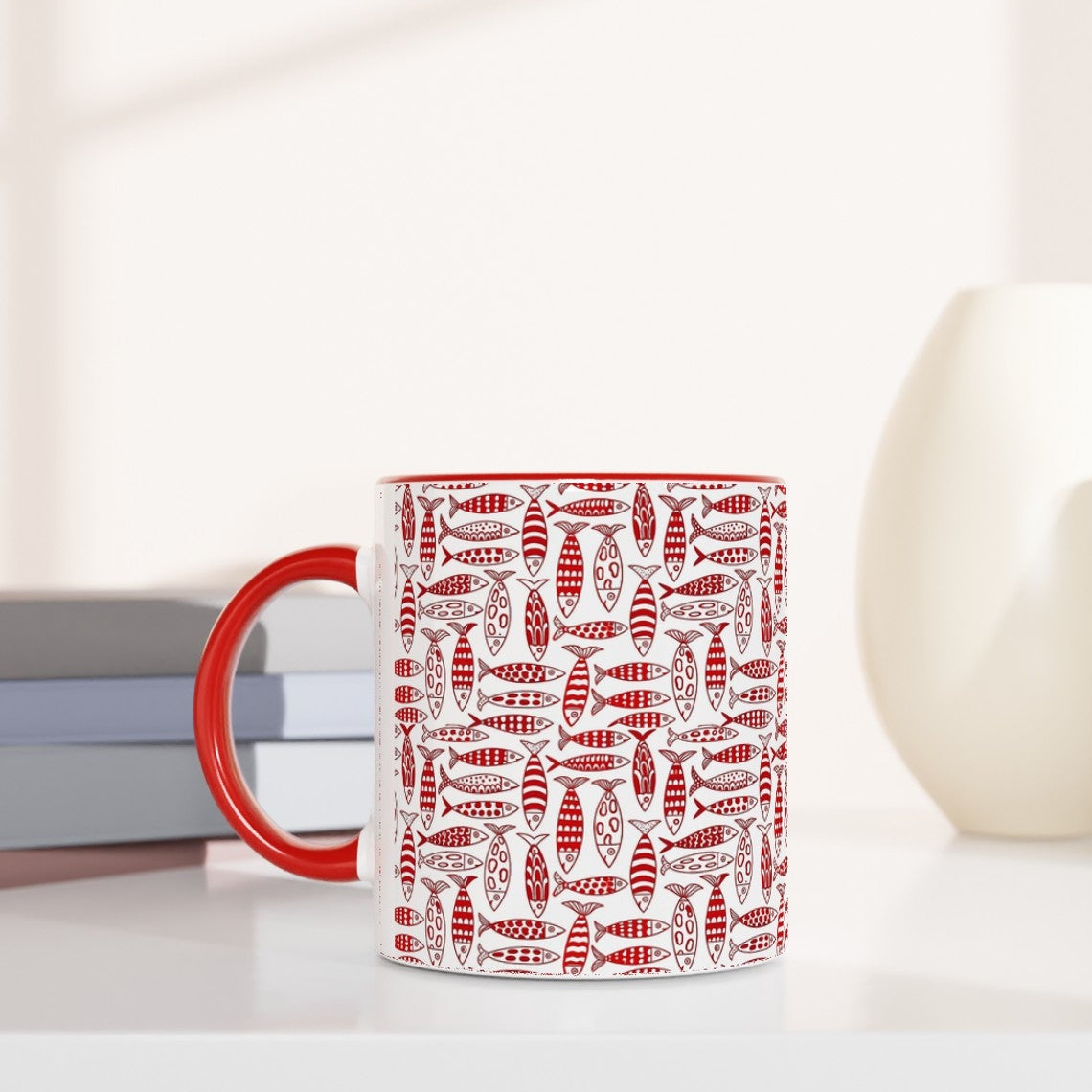 Red mug with white pattern on a white surface with books and decorative items.