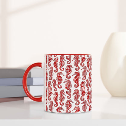 Red mug with seahorse pattern on a white surface with books and decorative items.