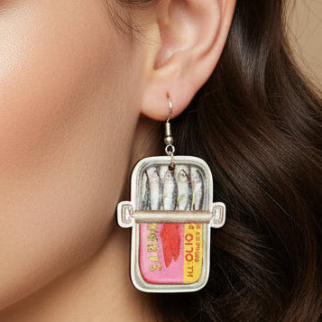 Sardine can earrings on a wooden surface