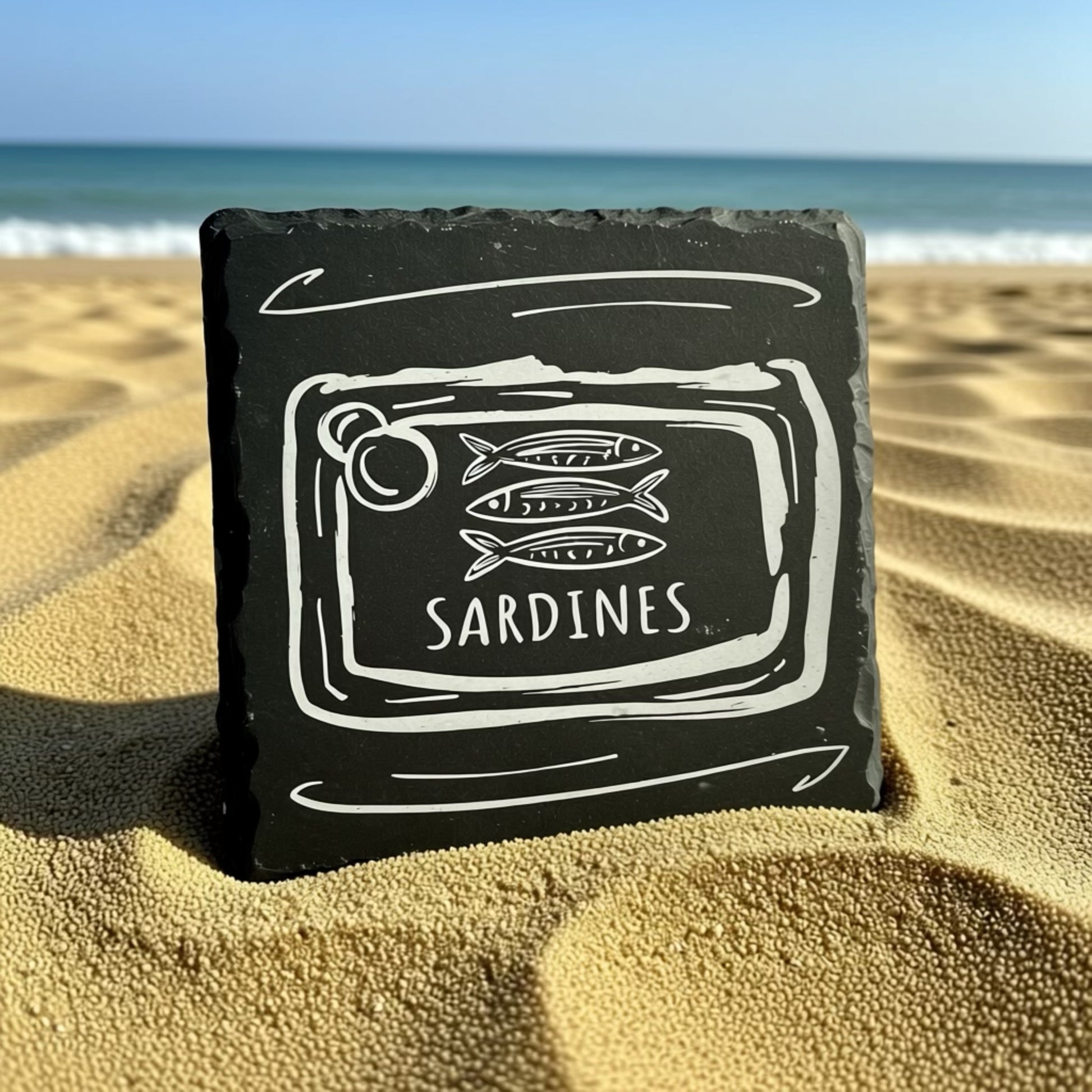Black slate with white line art of sardines and 'Sardines' text on a sandy beach.