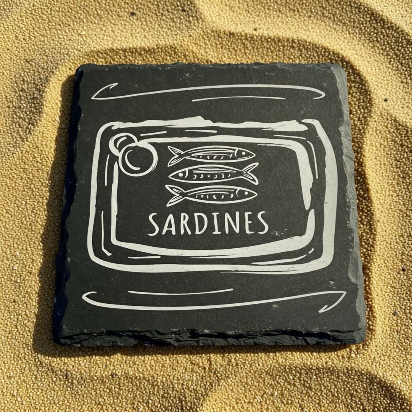 Slate coaster with sardine can design on a sandy background