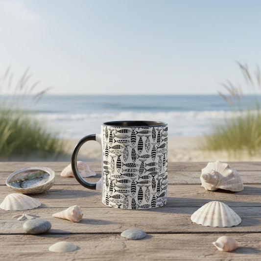 Black mug with fish pattern on a wooden surface near the beach
