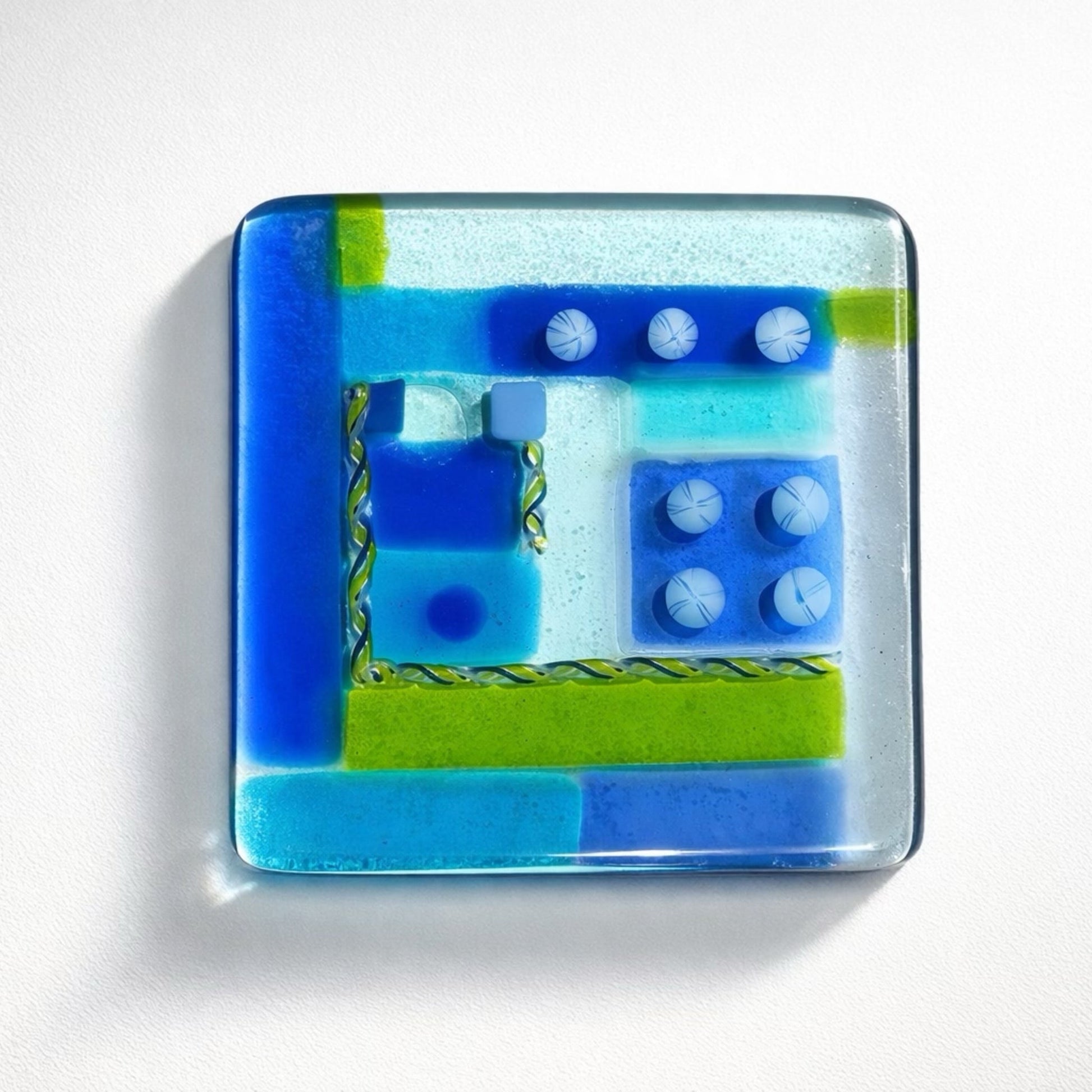 Square glass plate with blue and green geometric design on a white background