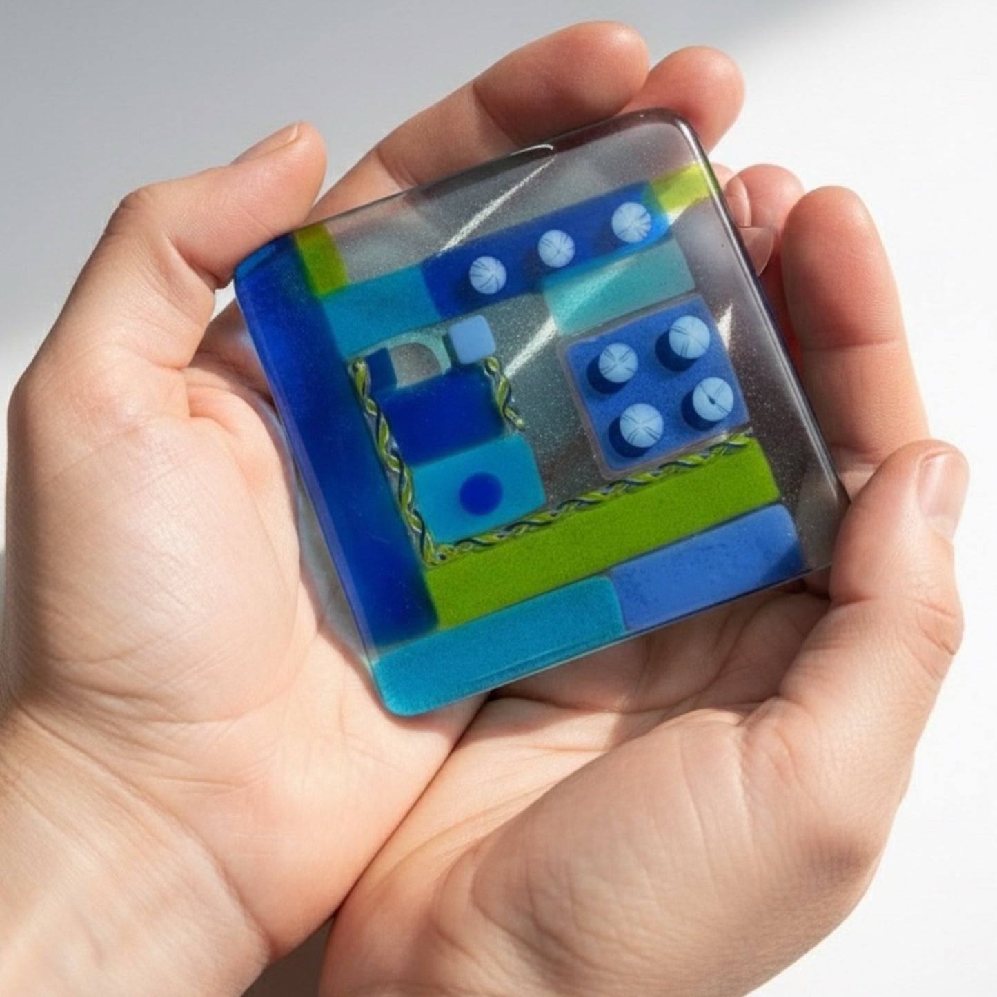 Hand holding a small, colorful rectangular object with a geometric design on a light background