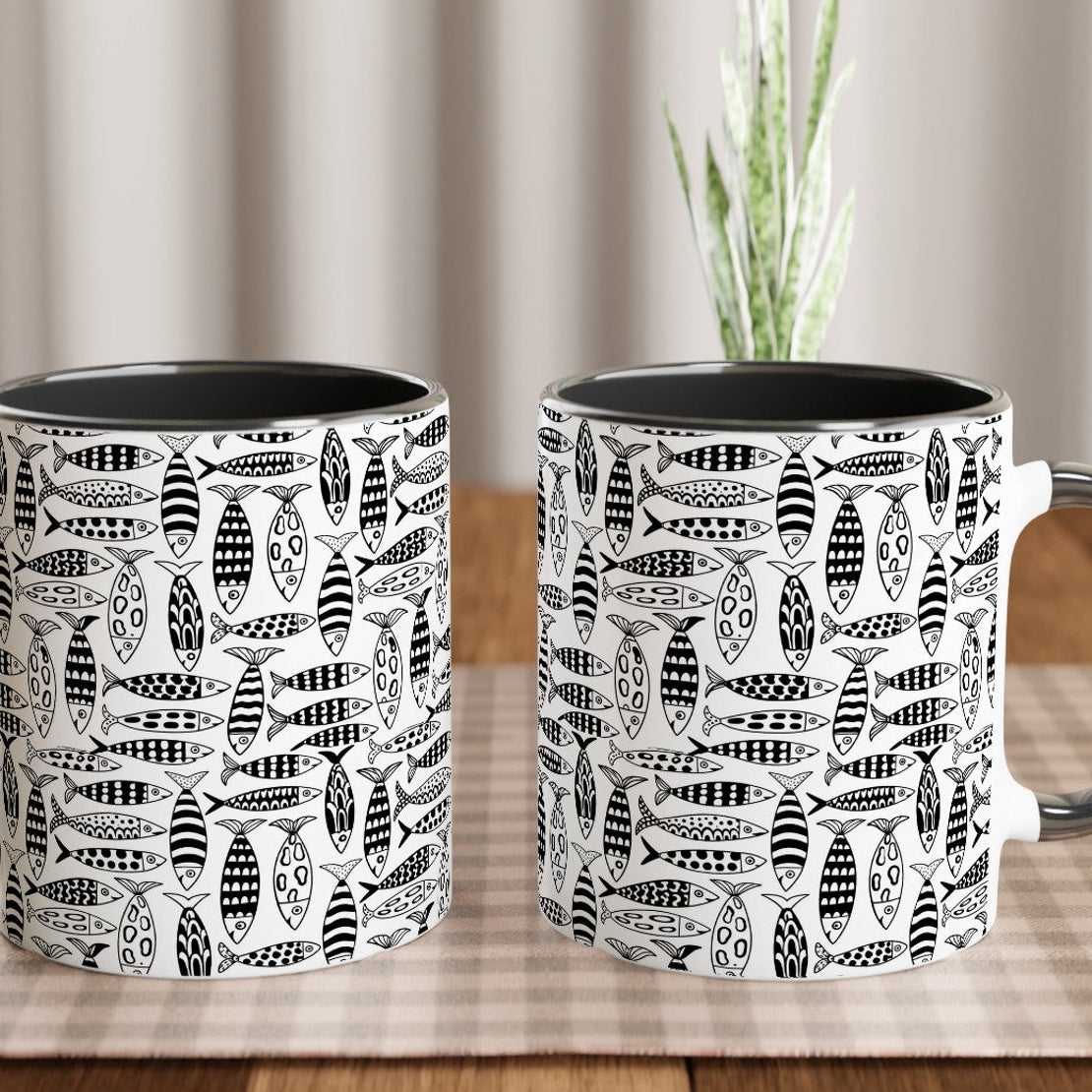 Two black and white patterned mugs on a wooden table with a plant in the background.