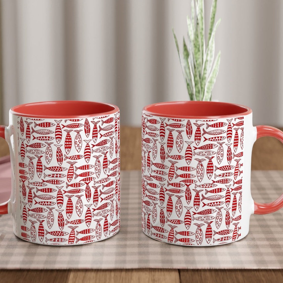 Two red and white patterned mugs on a wooden table with a checkered cloth.