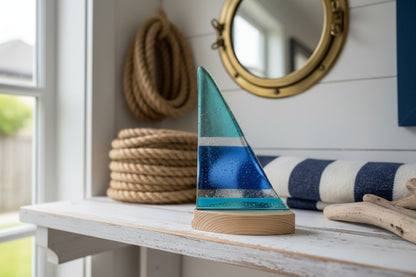 Glass sculpture resembling a sailboat on a white surface with a dark background
